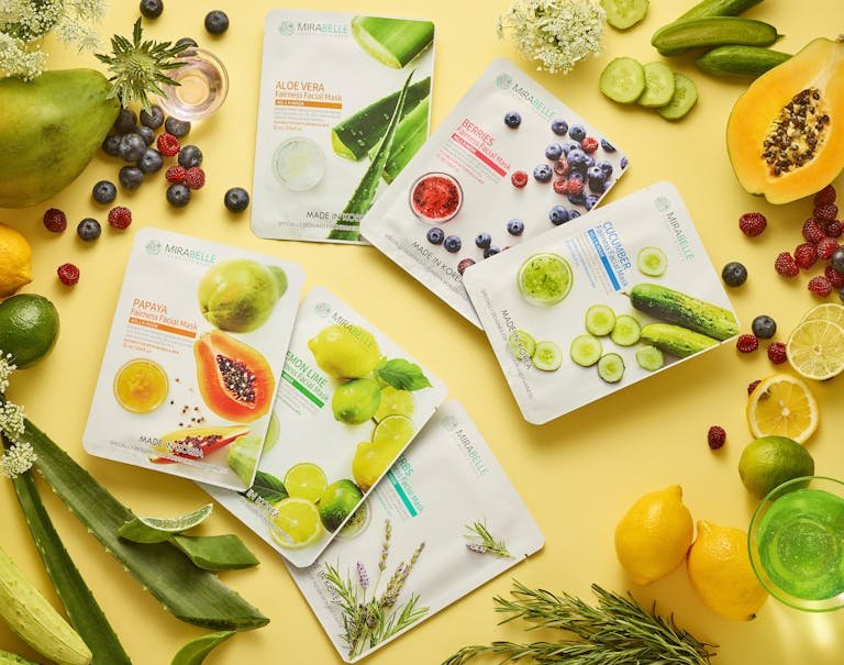 A collection of botanical face masks surrounded by fresh fruits and herbs on a yellow background.